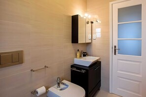 Ein modernes Badezimmer mit Toilette, Waschbecken und Spiegel. Über dem Spiegel befinden sich Lampen und eine Handtuchstange an der Wand.
