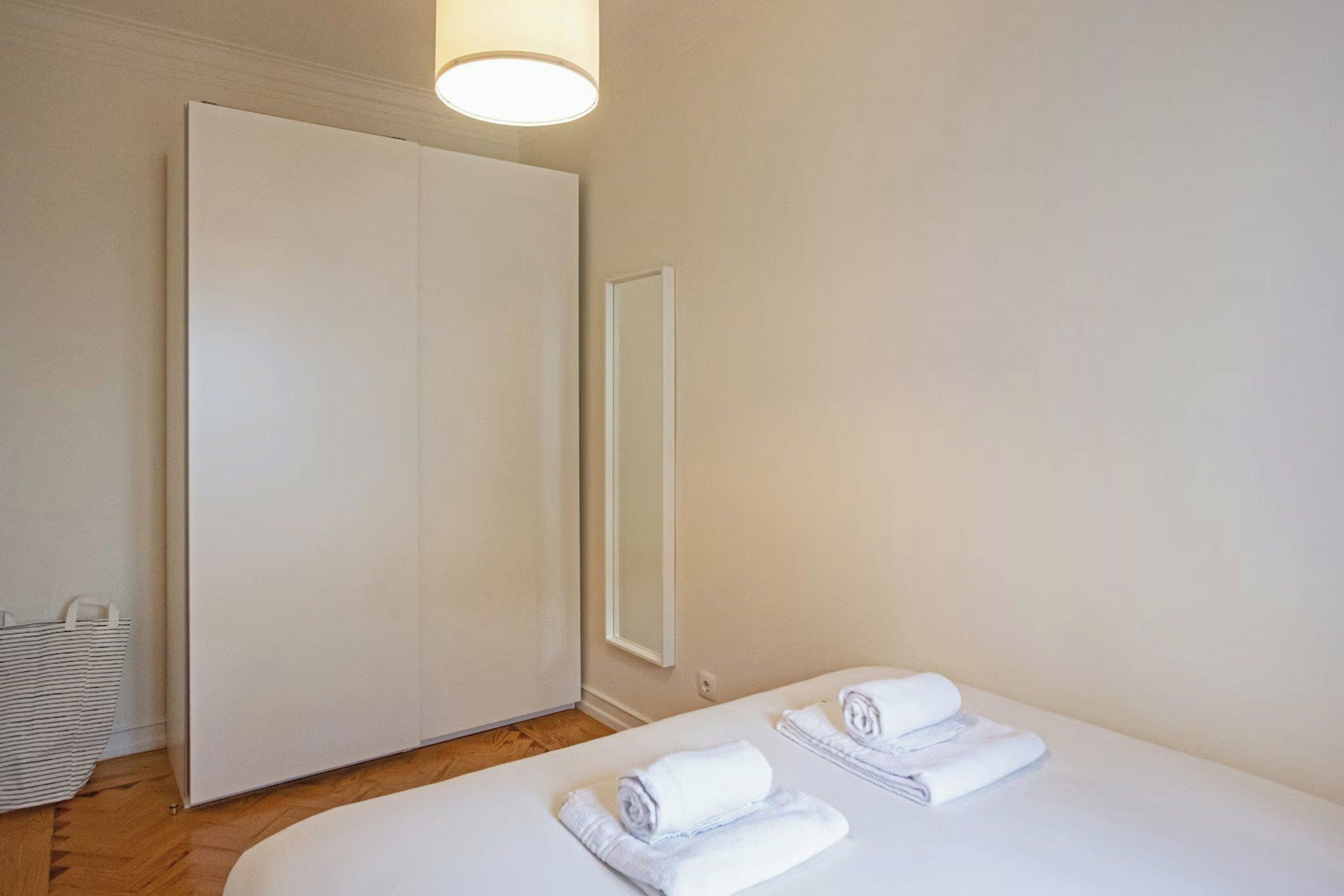 A hotel room with a bed, a wardrobe, a mirror, and a towel on the bed.