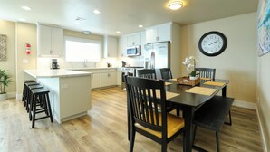 Une cuisine moderne avec des meubles blancs, un îlot central et un coin repas comprenant des chaises noires et une table en bois.