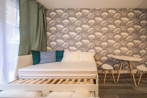 A bedroom with a bed, pillows, a small round table, and a wall with a leaf pattern. - Modern & Central Studio Home in Paris (Paris)