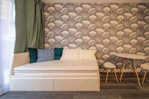 A bed with a white mattress, a green curtain, and a patterned wallpaper.