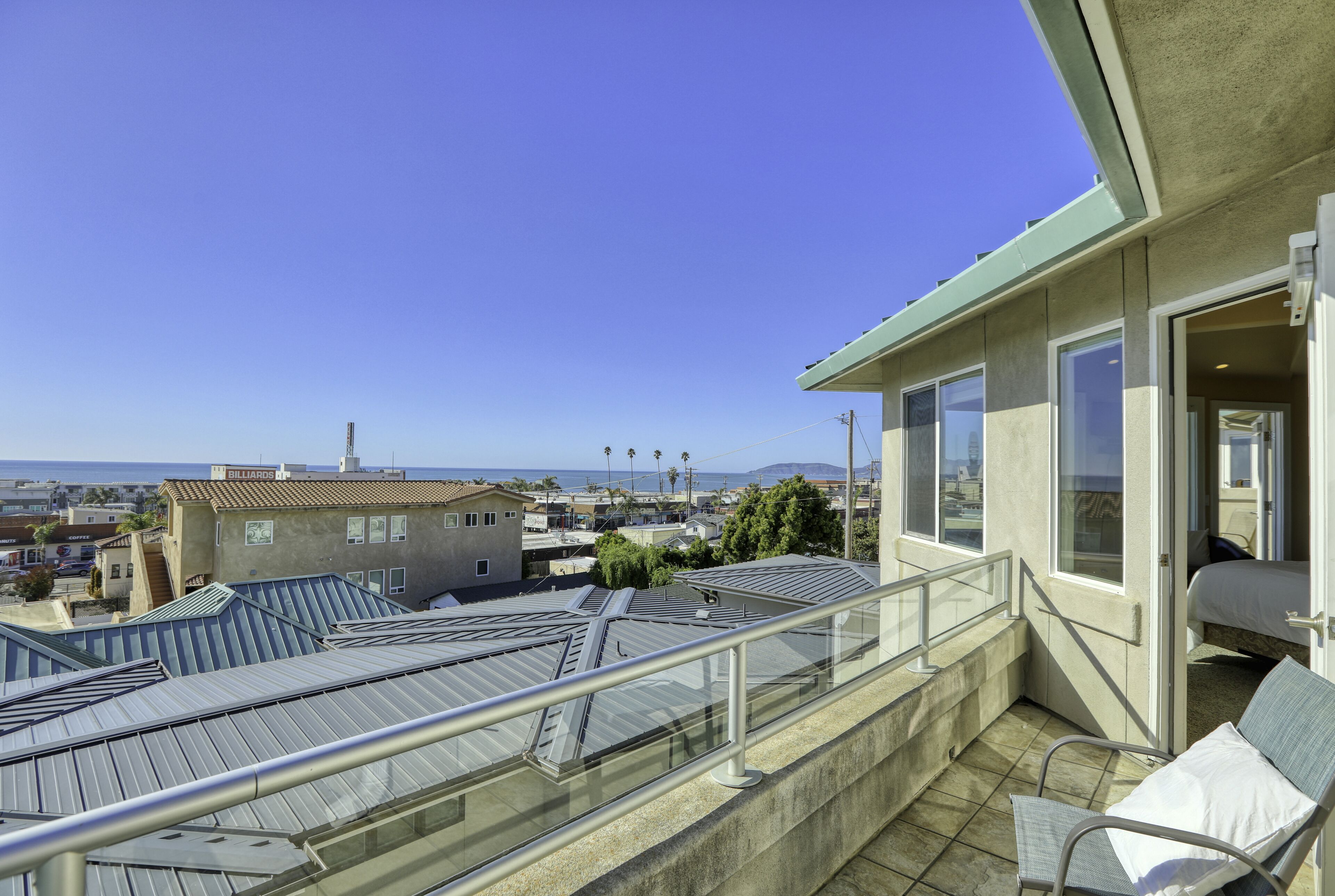 A balcony with a view of the city and ocean, a bed, and a chair.