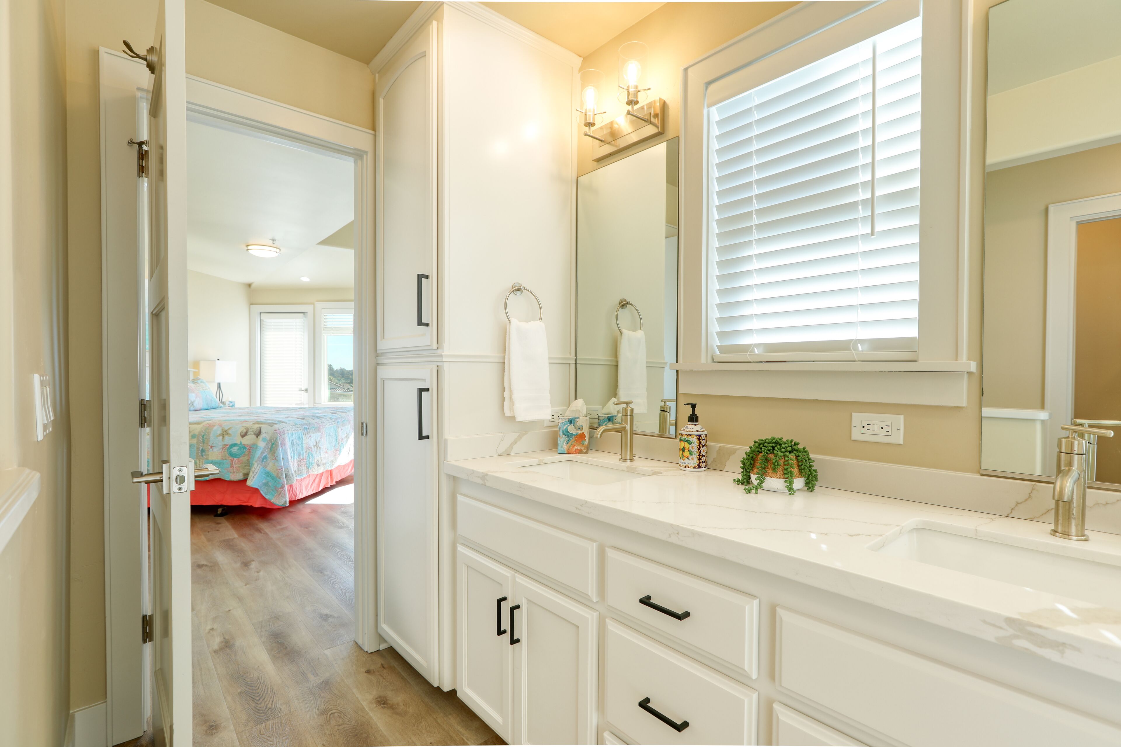A bathroom with a white vanity, a large mirror, and a window with blinds.