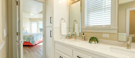 A bathroom with a white vanity, a large mirror, and a window with blinds.