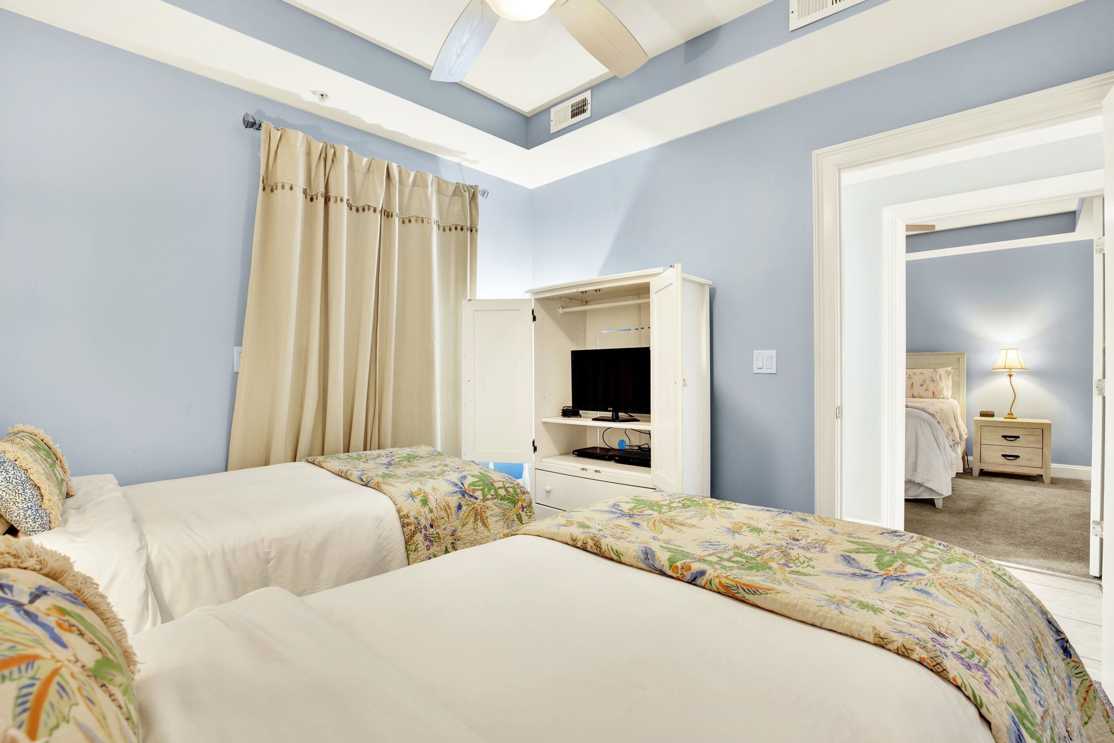 A bedroom with two beds, a wardrobe, a television, and a nightstand.