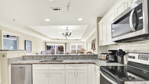 Una cocina moderna con armarios blancos, encimeras de granito, lavavajillas de acero inoxidable, horno empotrado y microondas.