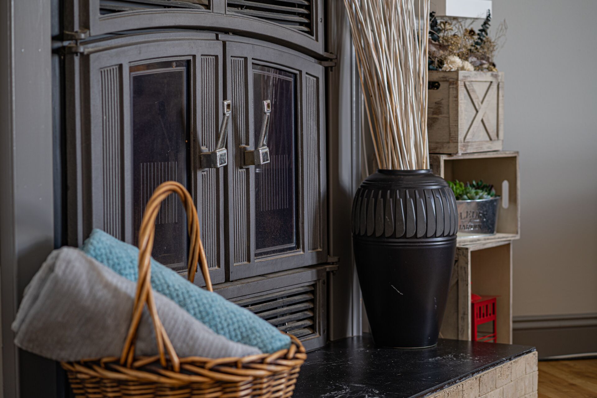 A wicker basket with folded towels, a black vase, and a wooden cabinet with a decorative handle.