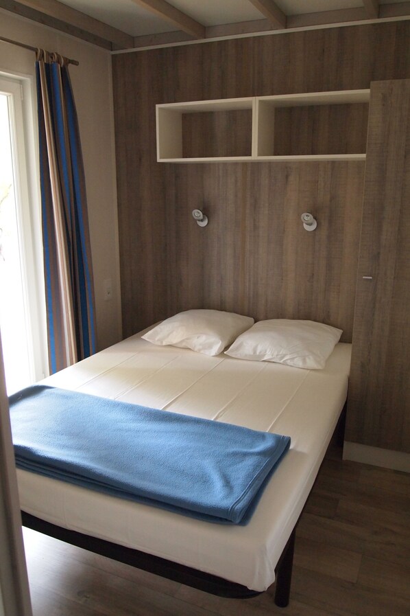 A bed with a blue blanket, wooden wall paneling, and a white headboard.