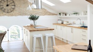A modern kitchen with a stone wall, pendant lights, and a large clock. - Luxury Penthouse - Luxury Cottages (Cheltenham)