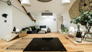 A modern kitchen with a black induction cooktop, wooden flooring, and hanging pendant lights. - Luxury Penthouse - Luxury Cottages (Cheltenham)