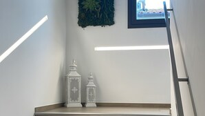 Una escalera con peldaños de madera, una planta verde colgada en la pared y dos faroles blancos.