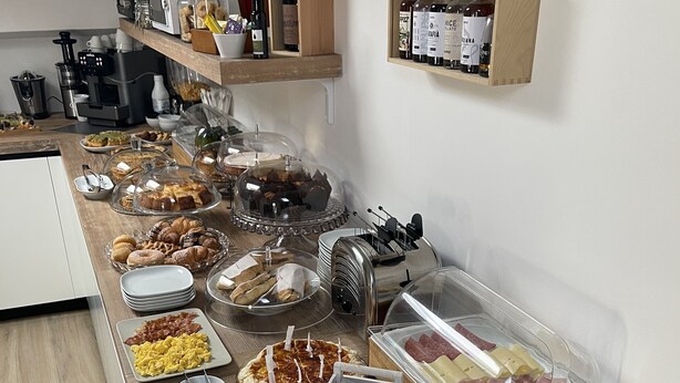Disposición de buffet con diversos alimentos, como pasteles, carnes y bebidas, sobre una encimera de madera.