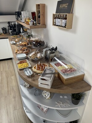 Ein reichhaltiges Buffet mit verschiedenen Speisen, darunter Gebäck, Fleisch und Getränke, auf einer Holztischplatte arrangiert.