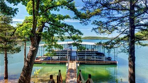 A dock leading to a glass-enclosed building with a view of a lake and distant hills. - Beaver Lake Cabin on the Waterfront with Boat Dock & Swim Deck (Eureka Springs)