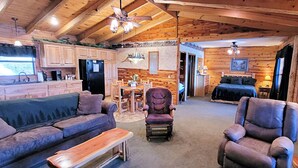 A cozy cabin interior with a dining area, a living room with a sofa and armchairs, and a bedroom with a bed and nightstand. - Beaver Lake Cabin on the Waterfront with Boat Dock & Swim Deck (Eureka Springs)