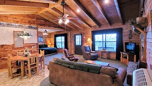 A cozy log cabin interior with a dining area, a living room with a sofa and chairs, a fireplace, and a television. - Beaver Lake Cabin on the Waterfront with Boat Dock & Swim Deck (Eureka Springs)