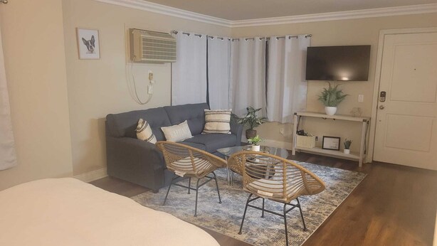 Een woonkamer met een grijze bank, twee rieten stoelen, een flatscreen televisie en een potplant.