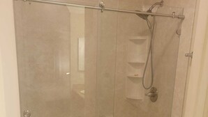 Een douchecabine met glazen wanden, een toilet en een klein plankje.