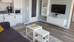 A modern living room with a sofa, a coffee table, a TV, and a kitchen area with appliances. - Holstenläger - close to the center (Grömitz)