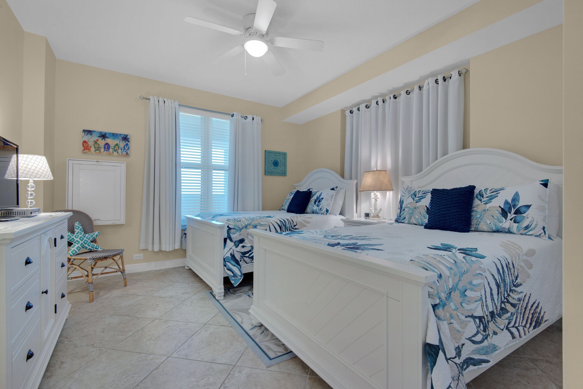 A bedroom with two beds, a ceiling fan, a desk with a lamp, and a chair.