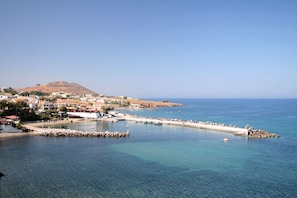Un pueblo costero con vista despejada al mar, una colina destacada al fondo y un muelle que se adentra en el agua.