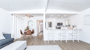 A modern, open-plan living and dining area with a kitchen, white furniture, and a ceiling fan.