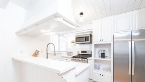 A modern kitchen with white cabinetry, a stainless steel refrigerator, a microwave, and a gas stove.