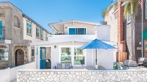 A two-story house with a stone wall in front, a blue door, and a patio area with a grill.