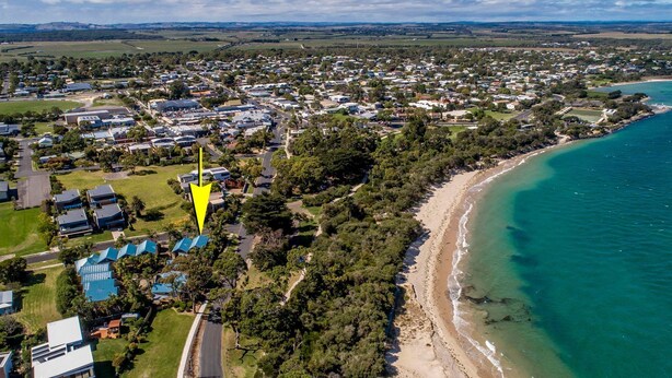 An aerial view of a coastal residential area with houses, a beach, and a large body of water. - In Da Block - Beachy Haven (Inverloch)