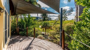 A wooden deck with a rope barrier, surrounded by lush greenery and a clear sky. - In Da Block - Beachy Haven (Inverloch)