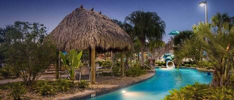 A pool area with a thatched-roof structure, palm trees, and a water slide.