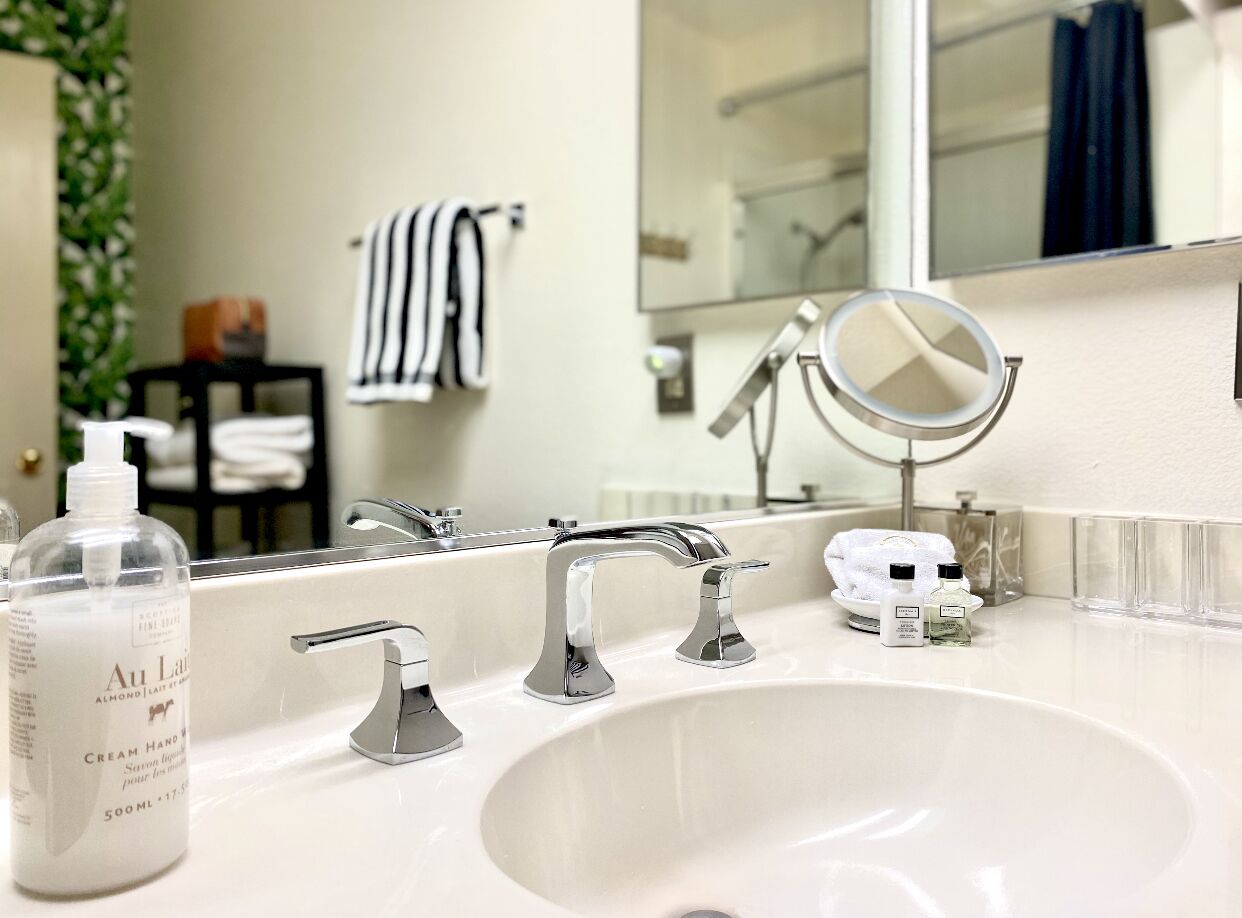 A bathroom with a white sink, two faucets, a mirror, and toiletries.