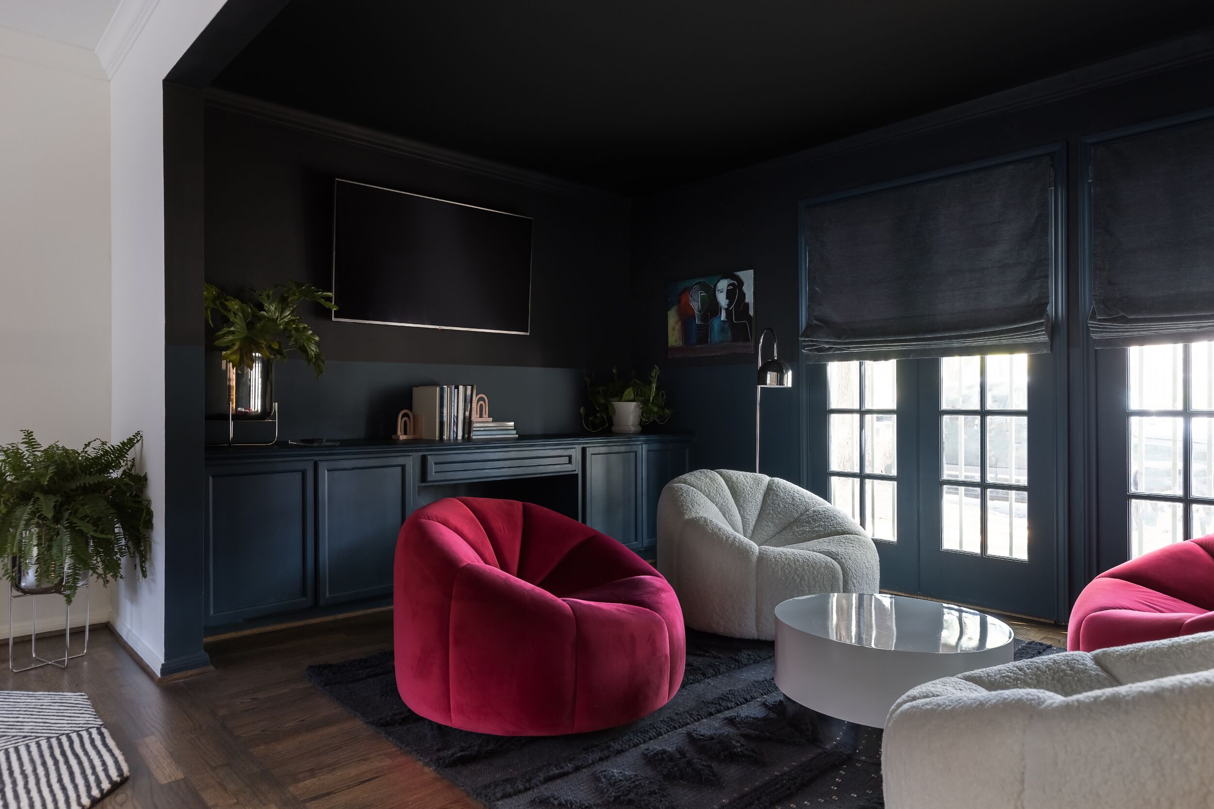 A modern living room with dark blue cabinetry, a flat-screen TV, and a large window with natural light.