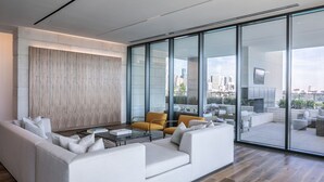 A modern living room with a sofa, coffee table, and chairs, large windows with a city view, and a wooden accent wall. - La Colombe d'Or Hotel (Houston)