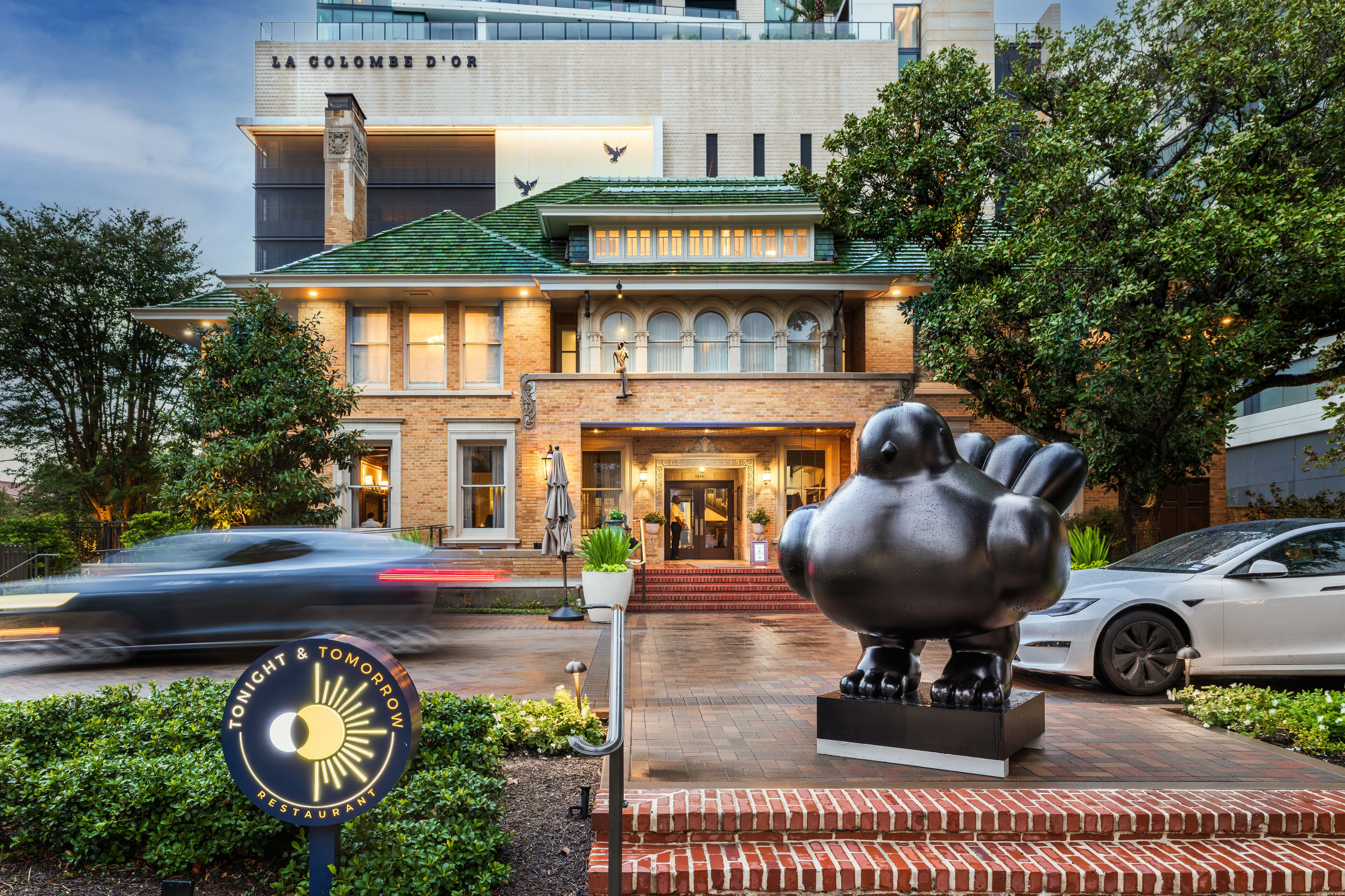 A hotel with a prominent entrance, a large sculpture in front, and a sign indicating it is a restaurant.