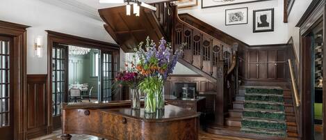 A grand lobby with a wooden reception desk, a staircase, and a chandelier.