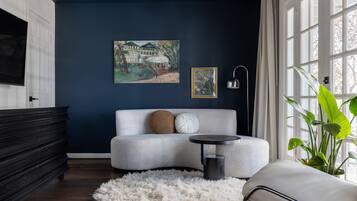 Un salón moderno con una pared azul oscuro, un sofá blanco, una mesa de centro redonda, una alfombra mullida y un ventanal con cortinas.