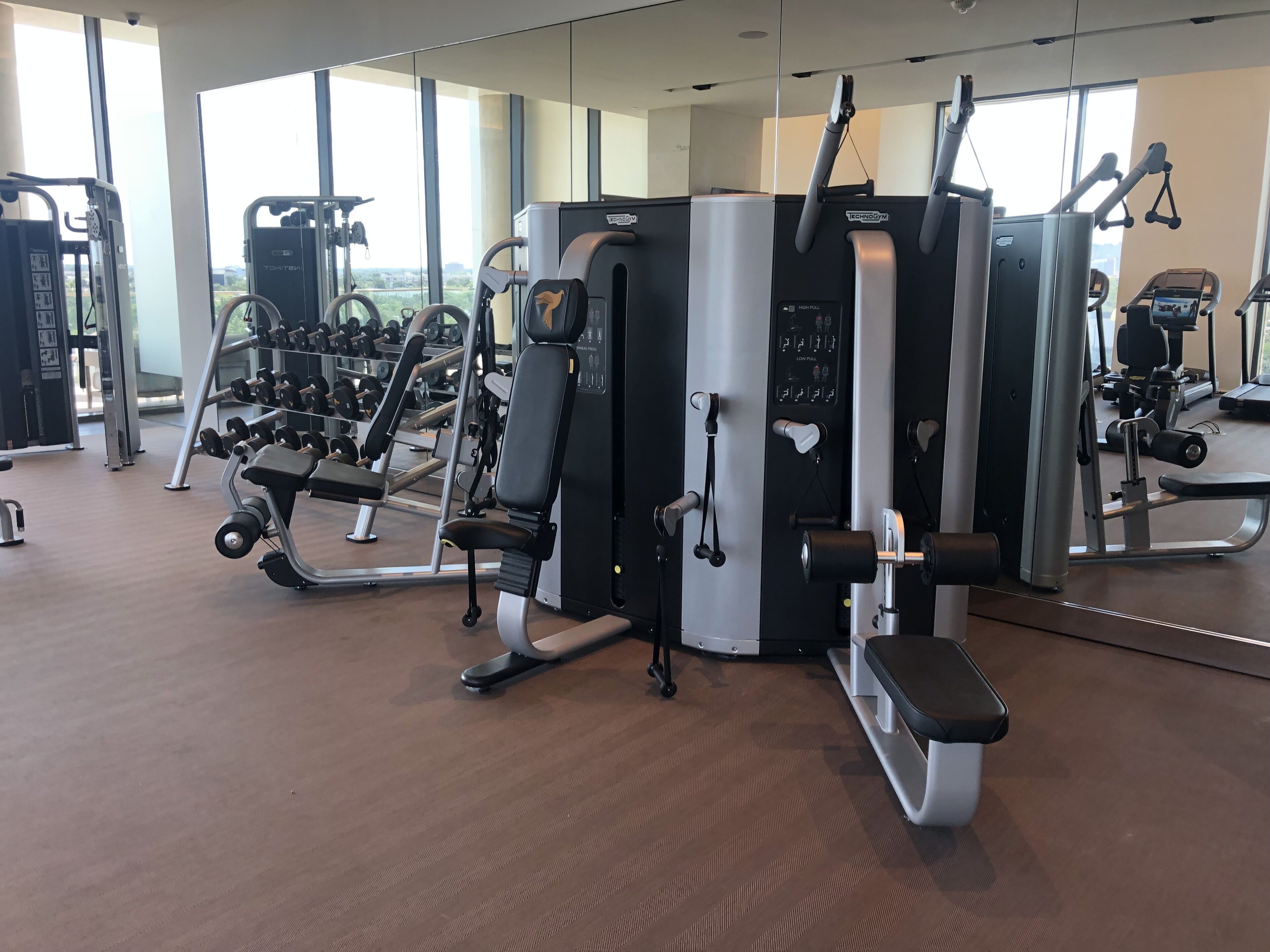A gym with various exercise machines, a bench, and dumbbells.