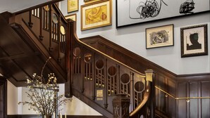A grand staircase with ornate woodwork, a chandelier, and a floral arrangement on a wooden table. - La Colombe d'Or Hotel (Houston)