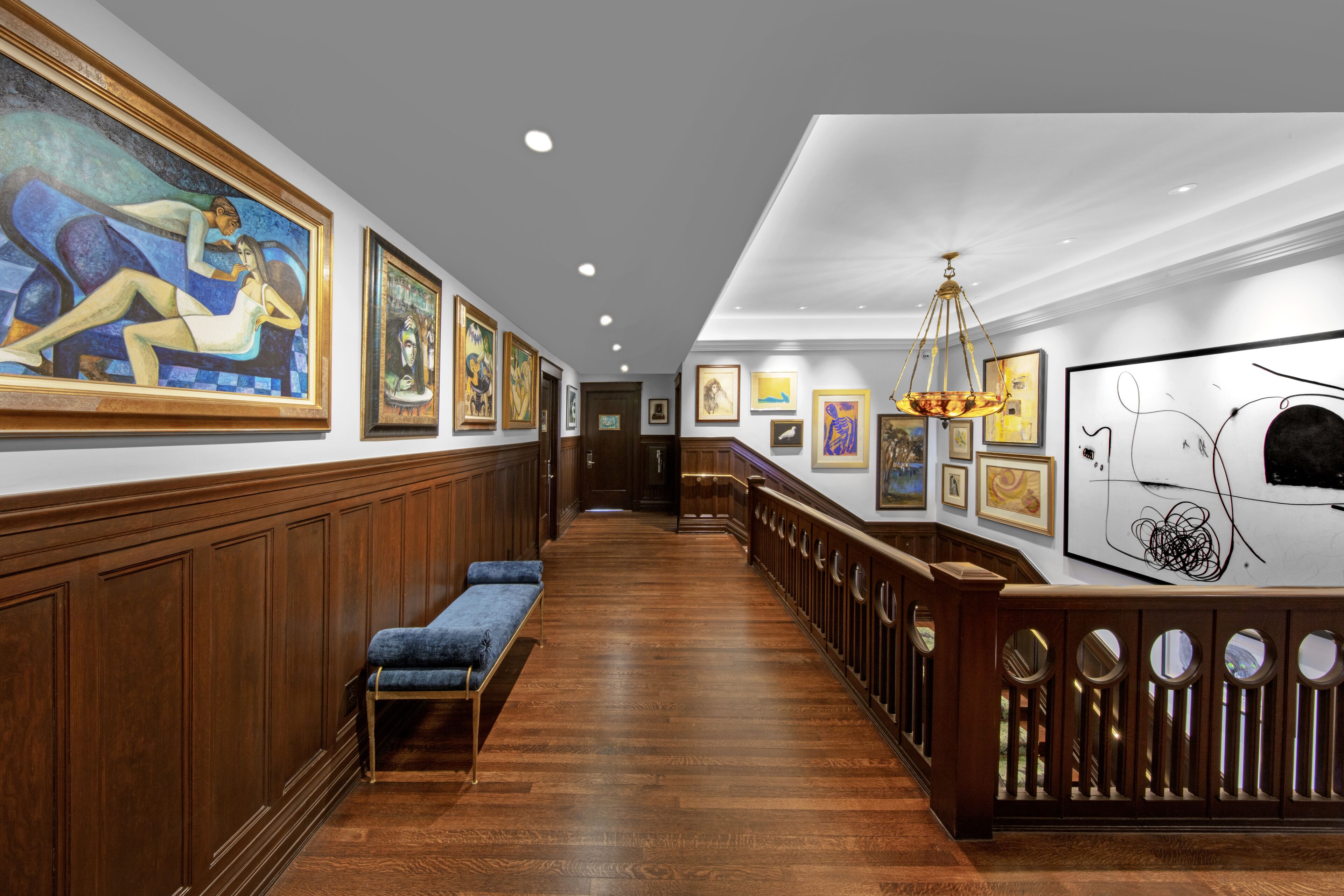 A hallway with wooden paneling, a blue bench, and framed artwork on the walls.