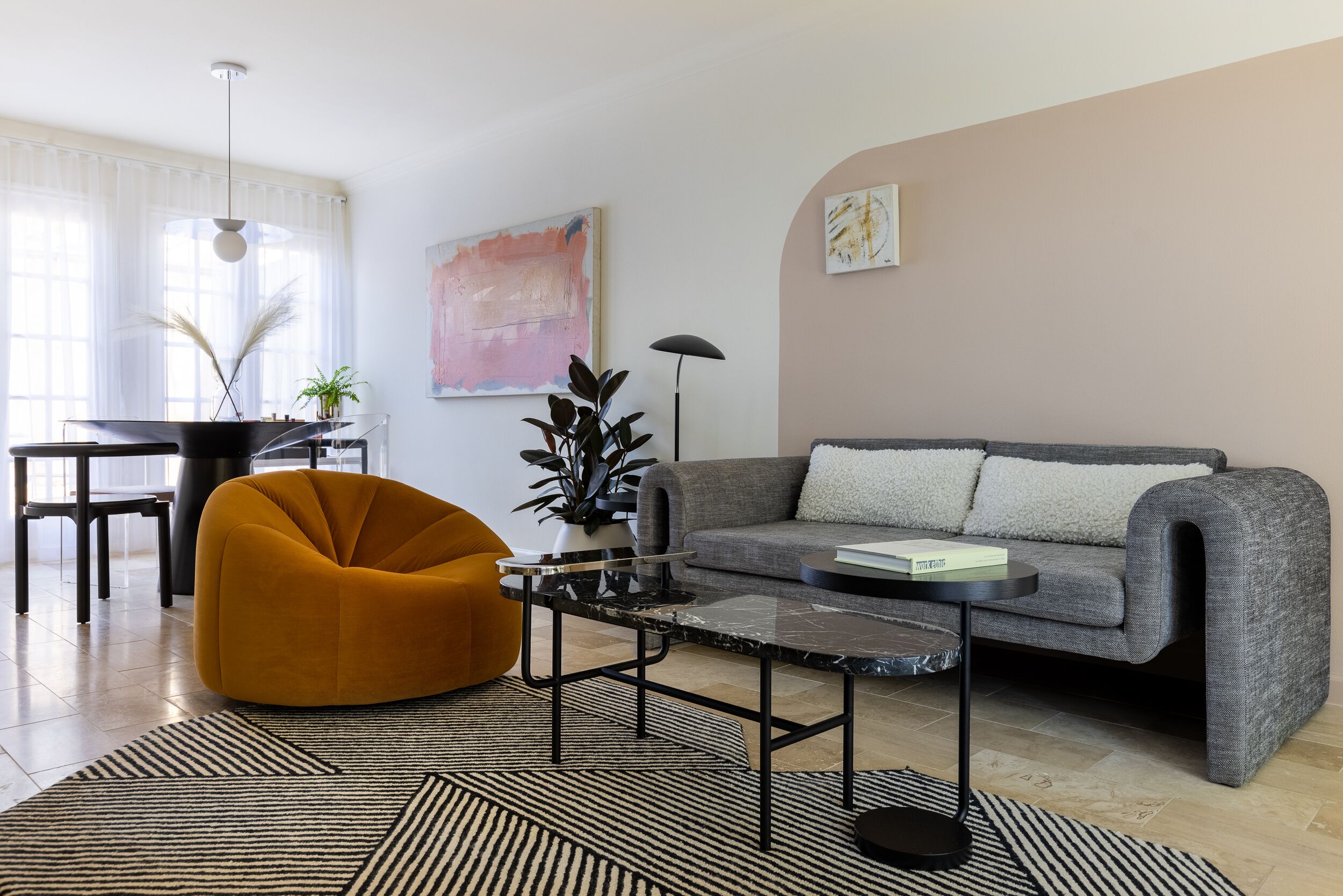 A modern living room with a sofa, a yellow chair, a coffee table, and a dining area with a table and chairs.