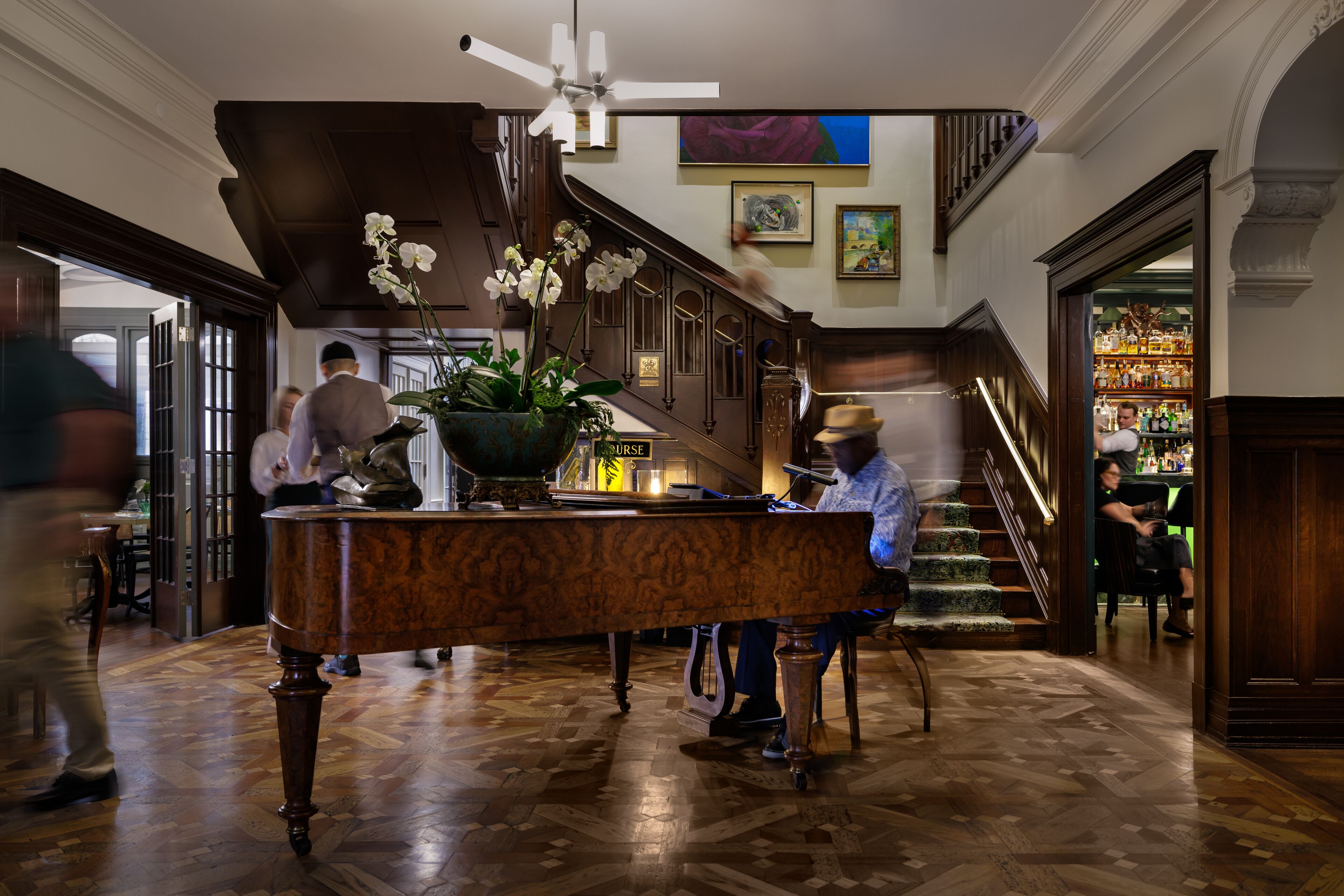 Un vaste hall d’entrée avec un piano, un escalier et un coin bar.