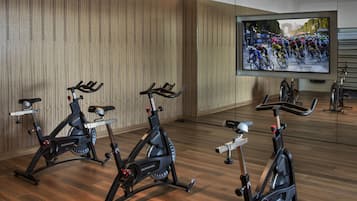 A gym with stationary bikes, a large screen displaying a cycling event, and wooden walls.