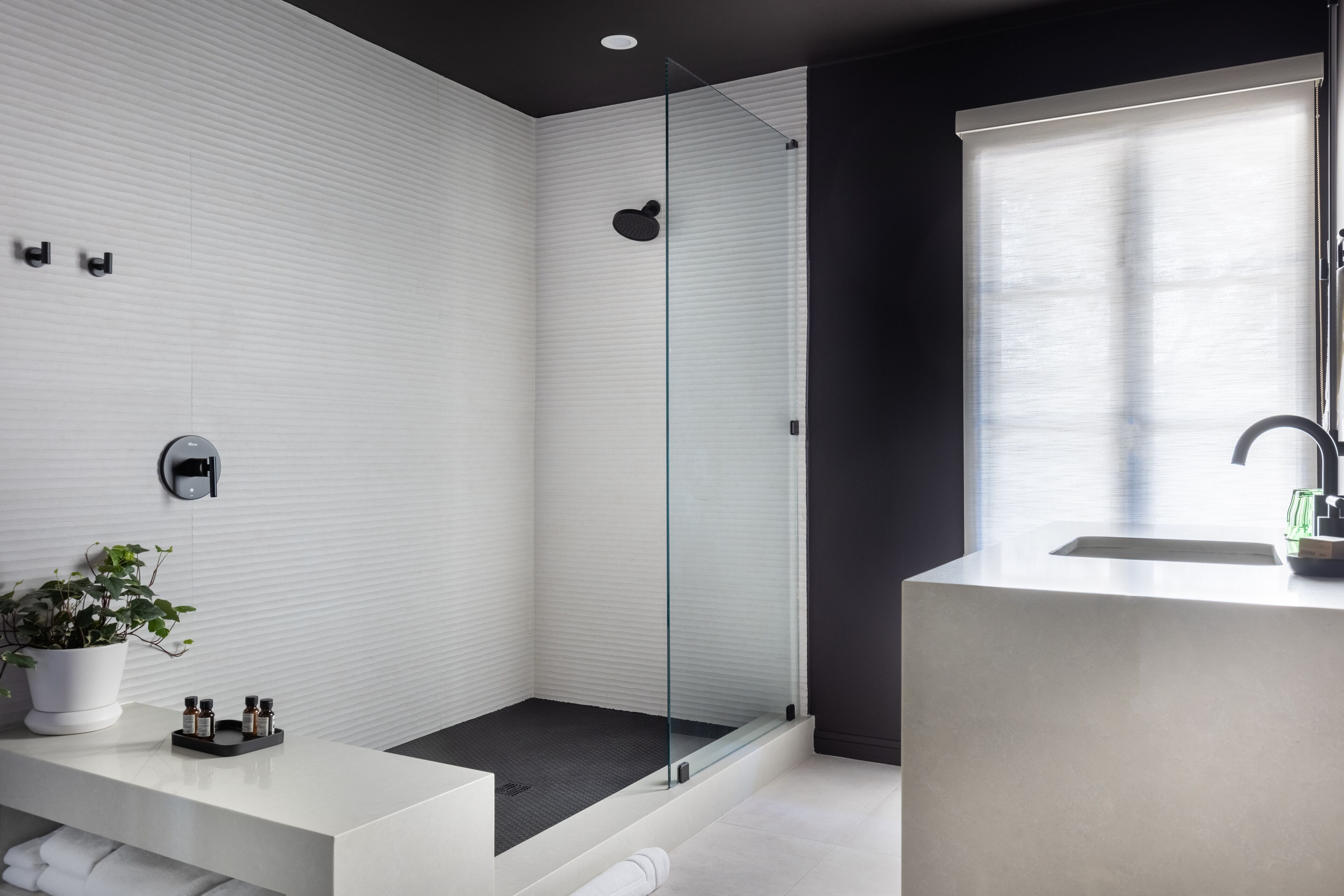 A modern bathroom with a glass-enclosed shower, a white vanity with a sink, and a potted plant.