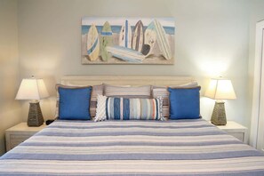 A bed with striped bedding, two blue pillows, and a painting of surfboards on the wall. - 2 The Sea |Steps to Private Beach | Community Pool (Santa Rosa Beach)