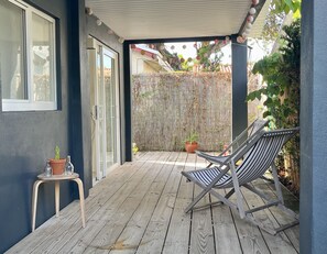 A wooden deck with a chair and a small table, a bamboo fence, and potted plants.