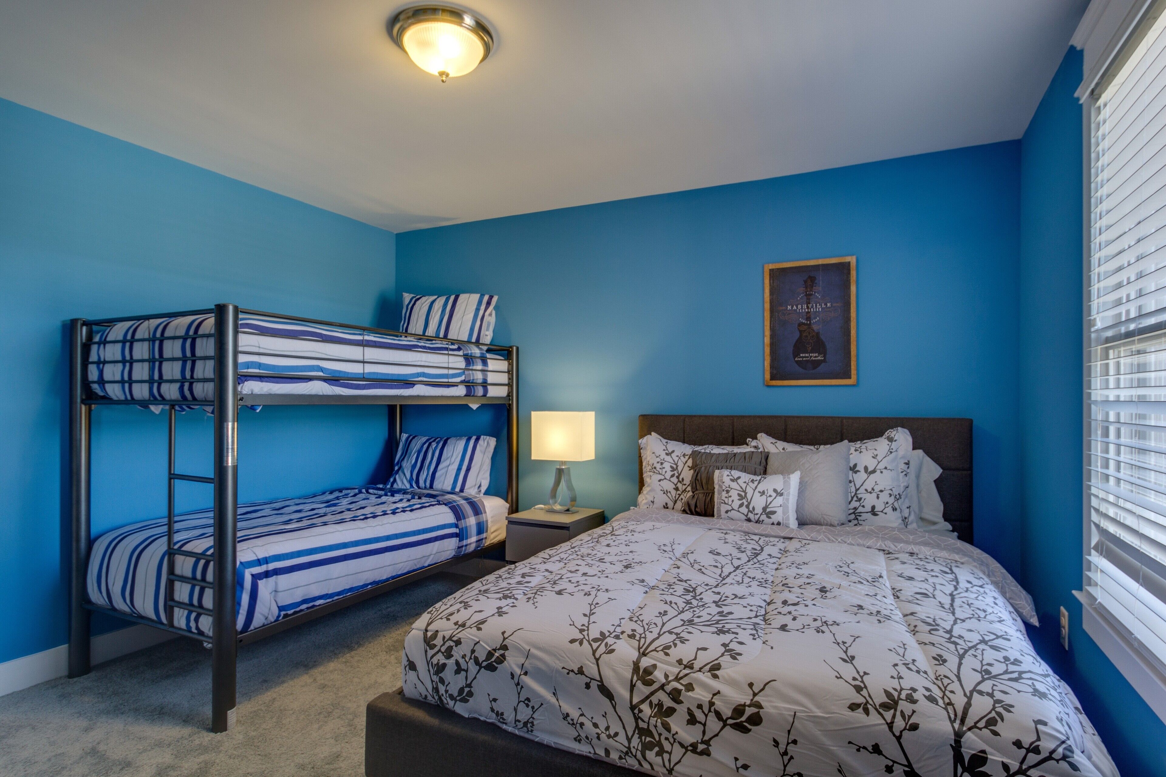 Un dormitorio con una cama litera, una cama individual y una mesita de noche con una lámpara.