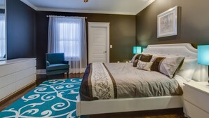 Een slaapkamer met een bed, een stoel, een plafondventilator, een deur en een nachtkastje.