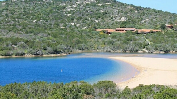 A coastal landscape with a sandy beach, a clear blue sea, and a hill with sparse vegetation. - Costa Serena, cottage near the sea. (Palau)