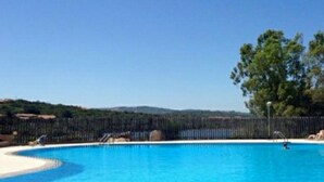 A clear blue swimming pool with a curved edge, surrounded by a fence and trees. - Costa Serena, cottage near the sea. (Palau)